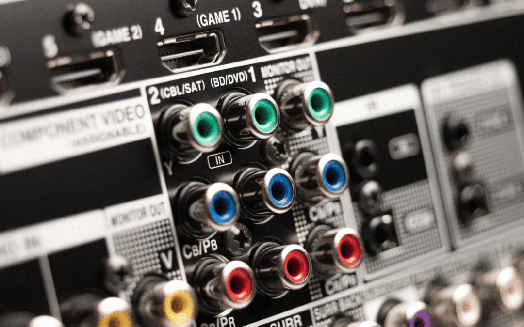 Close-up view of the rear panel of an AV receiver or home theater system, showing a variety of component video and audio input/output ports, including color-coded RCA jacks and HDMI connections labeled for different devices like DVD, SAT, and game consoles.