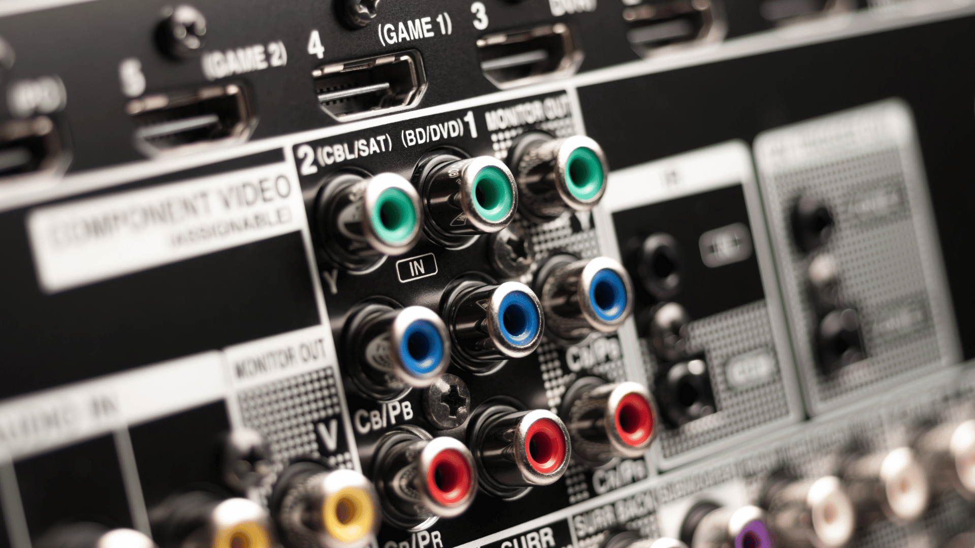 Close-up view of the rear panel of an AV receiver or home theater system, showing a variety of component video and audio input/output ports, including color-coded RCA jacks and HDMI connections labeled for different devices like DVD, SAT, and game consoles.