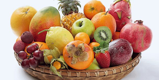 A wicker basket filled with a colorful variety of fresh fruits including pineapple, kiwi, mango, pomegranate, dragon fruit, grapes, oranges, lemons, persimmon, strawberry, apple, lychee, and passion fruit.