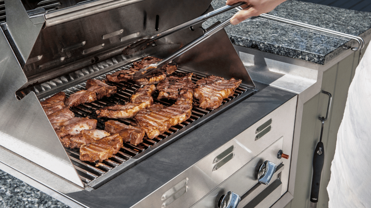 Person grilling marinated ribs on a stainless steel outdoor gas barbecue grill with tongs.