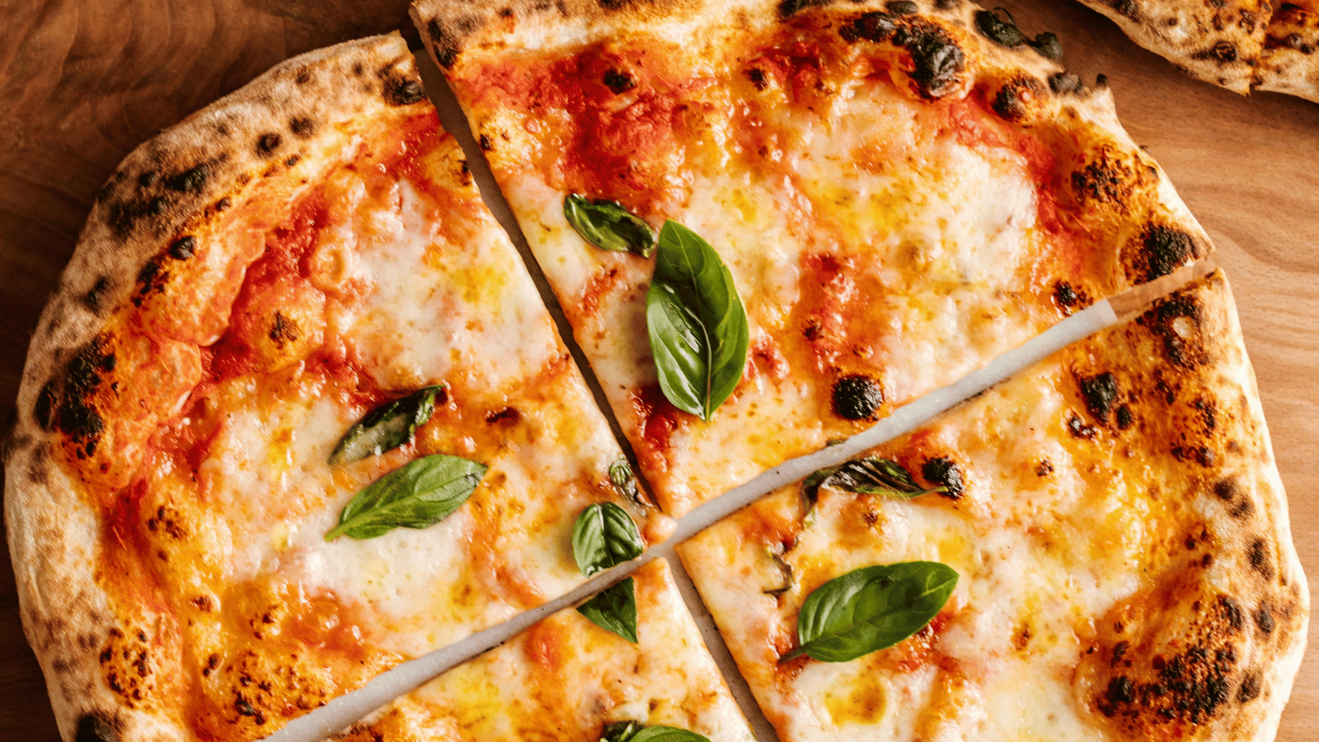 Close-up of a freshly baked sliced Margherita pizza with a crispy crust, melted mozzarella, tomato sauce, and fresh basil leaves on a wooden surface