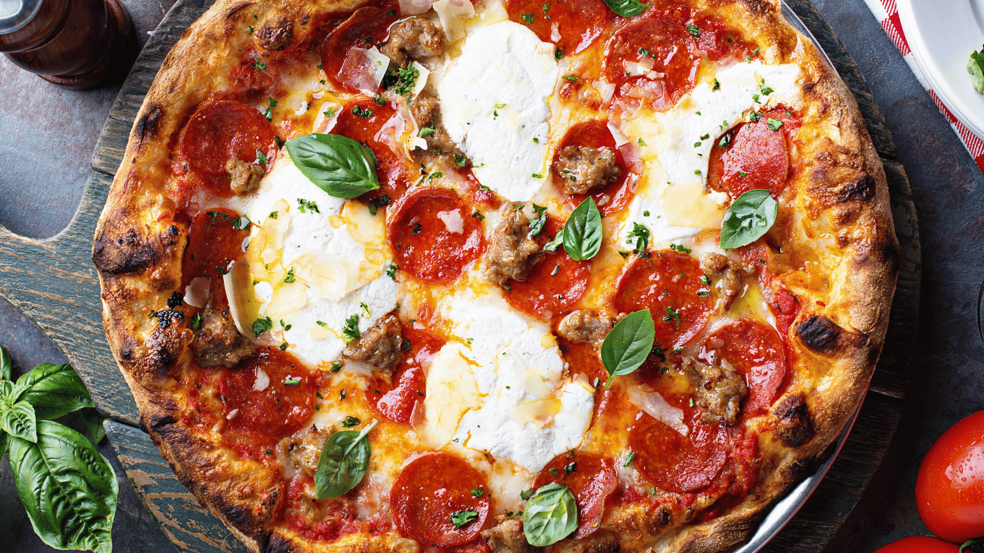 Freshly baked pepperoni pizza topped with dollops of ricotta cheese, sausage, and fresh basil leaves, served on a wooden board.