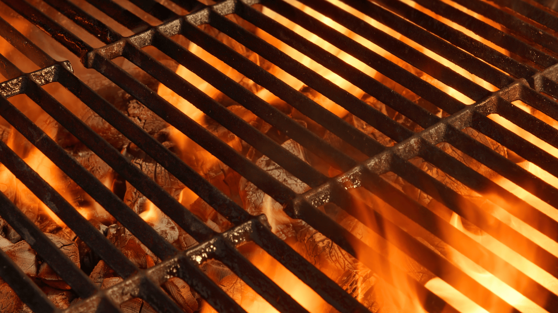 Close-up view of a hot barbecue grill with flames and glowing charcoal beneath the metal grates, ready for outdoor cooking.
