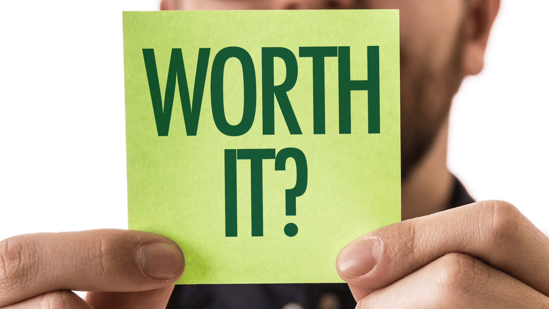 Close-up of a person holding a green sticky note with the bold text "WORTH IT?" written in dark green letters.