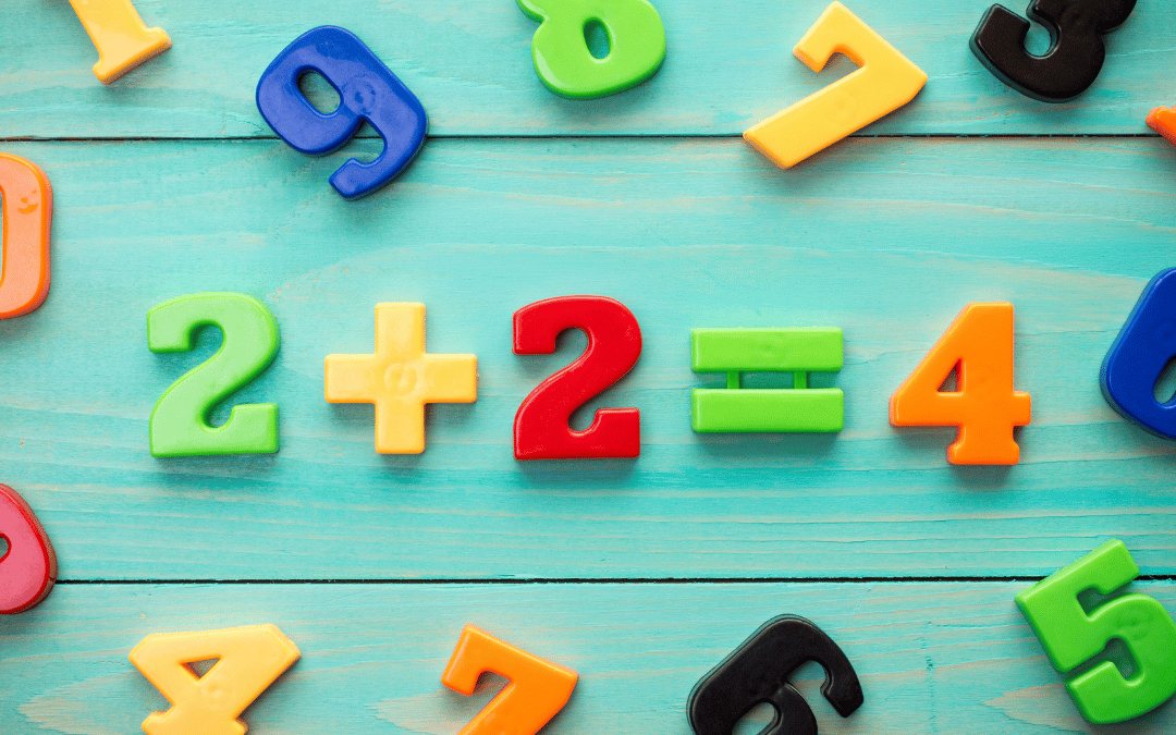 Colourful plastic numbers and math symbols on a turquoise wooden surface form the equation "2 + 2 = 4", surrounded by scattered digits in various colours.
