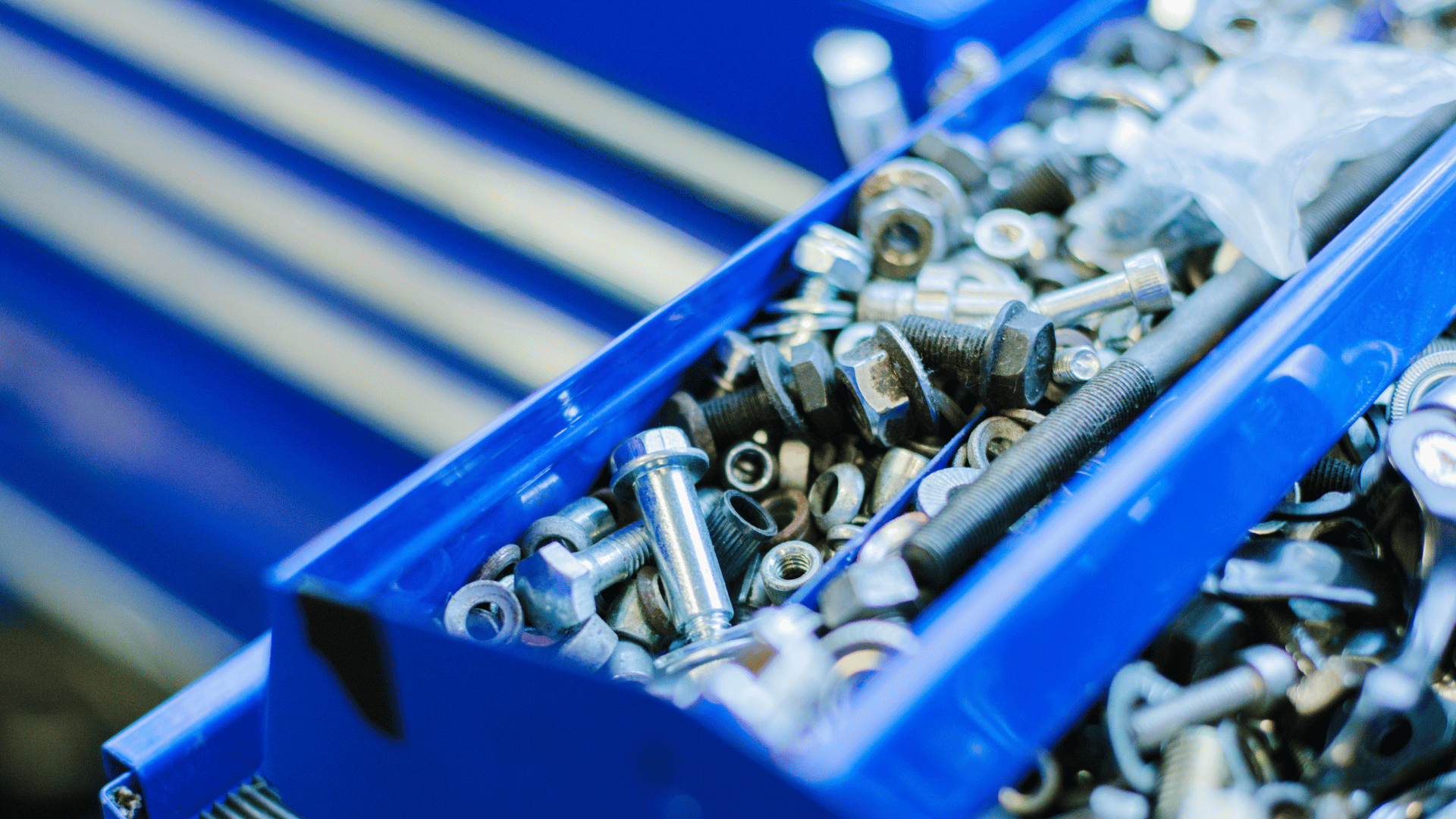 Close-up of an open bright-blue tool-chest drawer filled with assorted metal bolts, nuts, washers, and screws, captured with shallow depth of field.