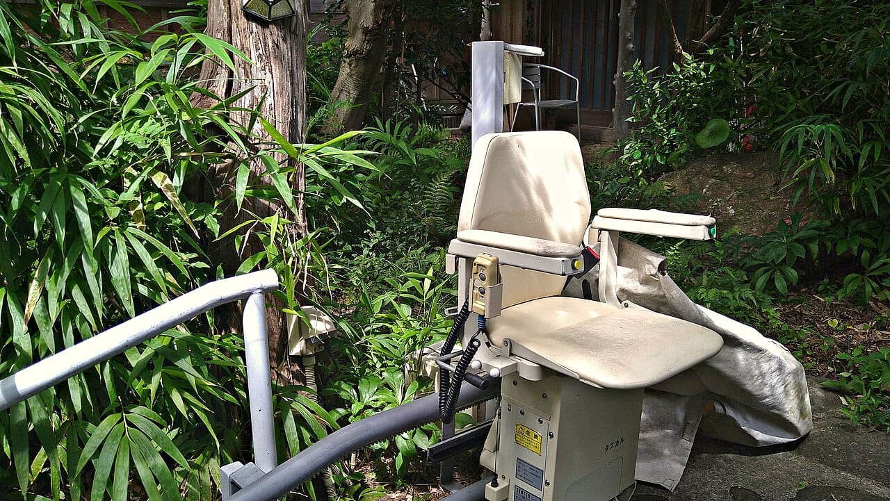 A chair-type stairlift folded at the bottom of a staircase