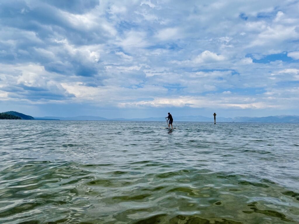 A person stand-up paddleboarding on calm clear water on a bright summer day