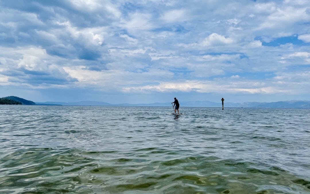 A person stand up paddleboarding on calm clear water