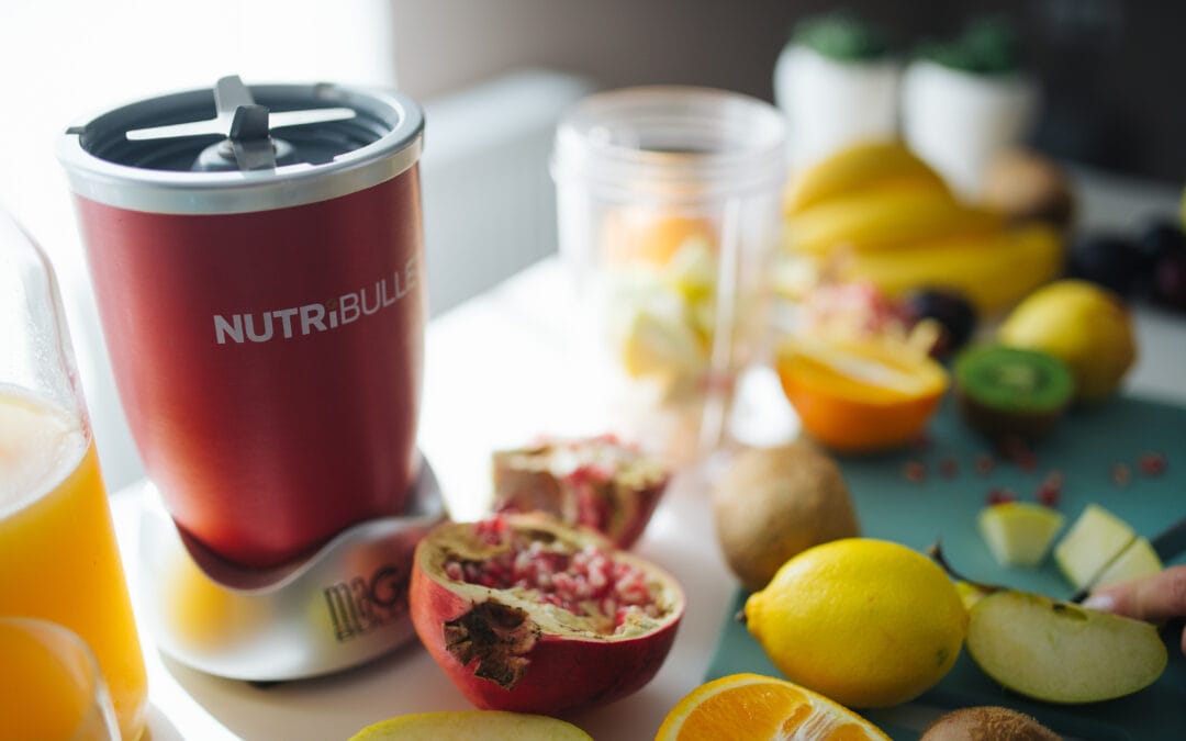 A portable blender on a kitchen counter surrounded by fresh fruit ready for a smoothie