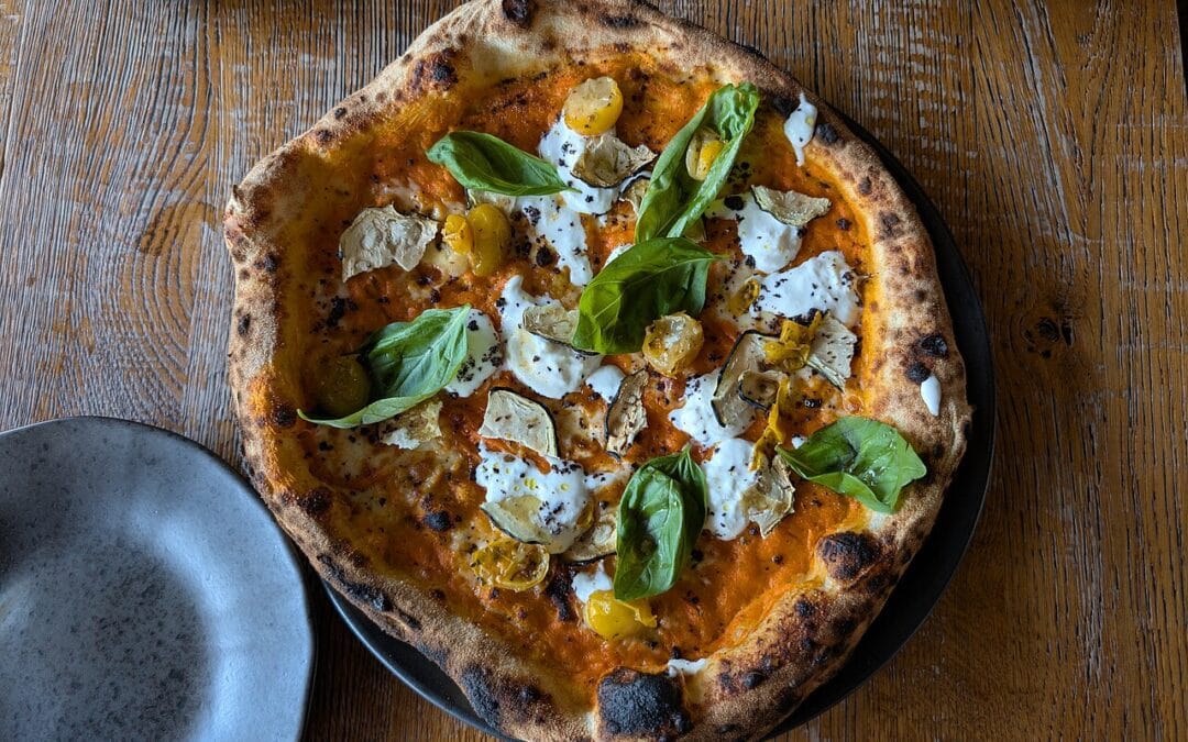 A leopard-spotted wood-fired pizza topped with basil, fresh from a hot pizza oven