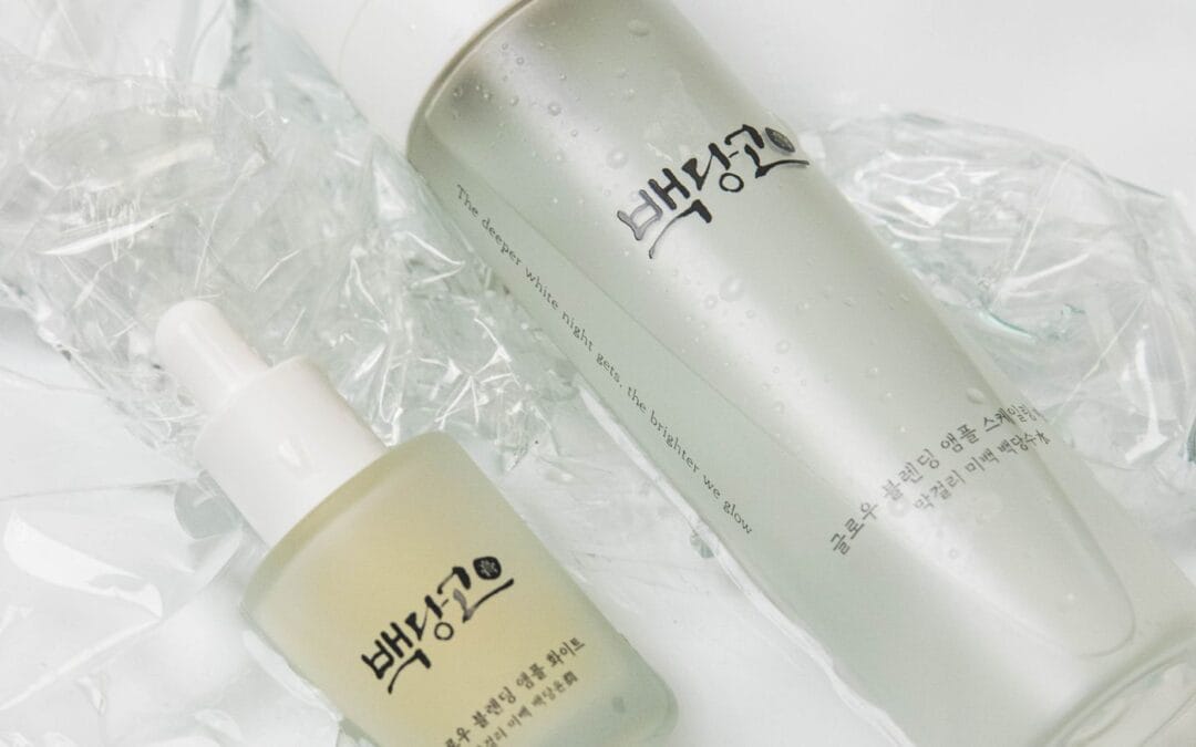 Two Korean skincare bottles, a glass ampoule dropper and a toner, photographed on a white surface