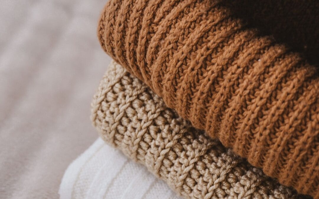 A neat stack of folded chunky knit jumpers in warm autumn colours, ready to be packed away in vacuum storage bags