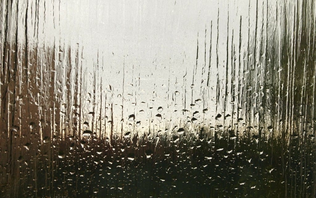 Heavy condensation and water droplets running down the inside of a cold window pane