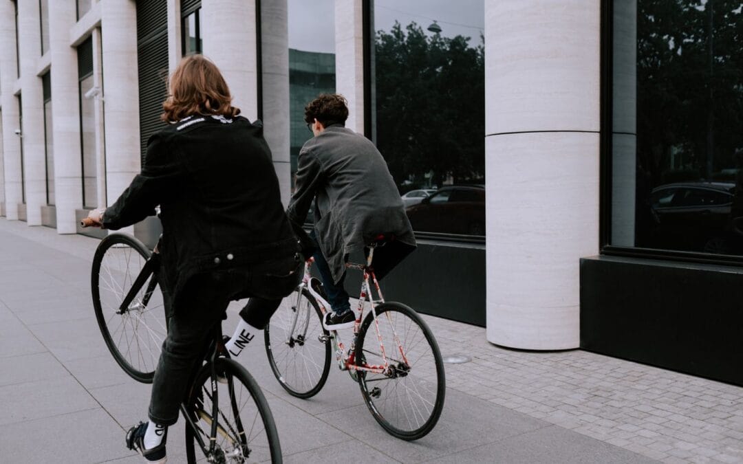 Two people riding bikes along a city pavement in low evening light