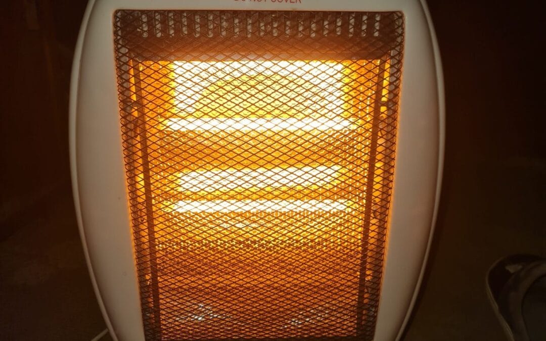 A white portable halogen electric heater switched on in a dark room, its three bars glowing orange behind the guard