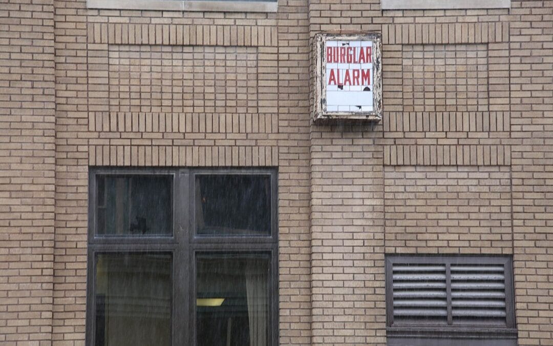 A burglar alarm bell box mounted on the brick wall of a UK house above a window