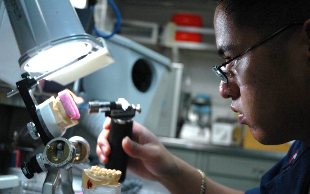 A dental technician shapes a custom-made mouth guard on a dental model at a laboratory bench