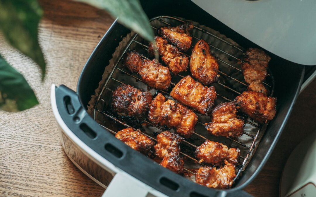 Open air fryer drawer with the crisper plate visible and cooked chicken pieces inside
