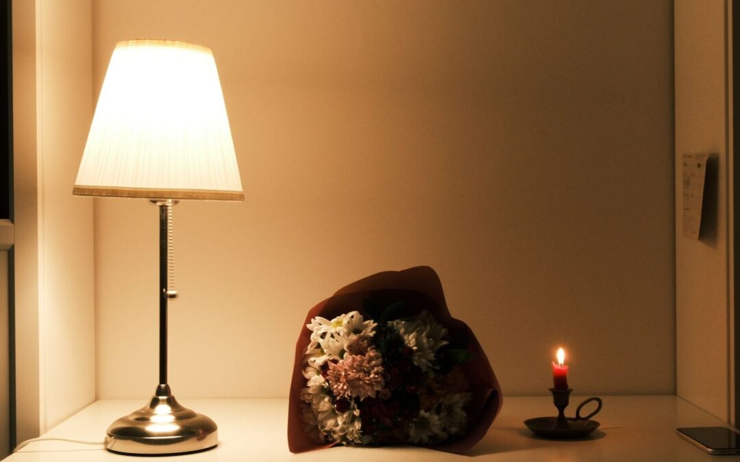 Warm table lamp glowing beside a bouquet and a small candle on a sideboard