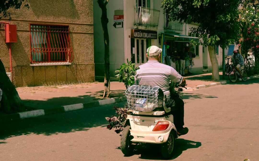 A man riding a small mobility scooter along a sunny street