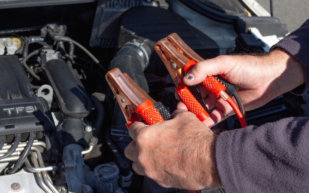 Hands holding jump starter clamps over a car engine bay