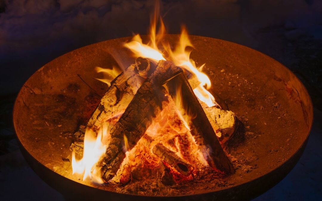 Glowing campfire with burning logs inside a round metal fire pit at night