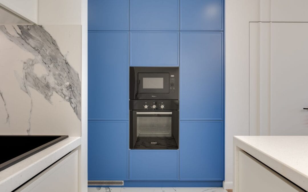 A built-in microwave above an electric oven in a blue kitchen unit, with a hob in the foreground