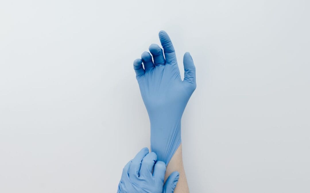Hands pulling on a blue disposable nitrile glove against a pale background