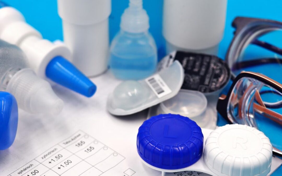 Dropper bottles of eye drops beside a contact lens case, a prescription and a pair of spectacles