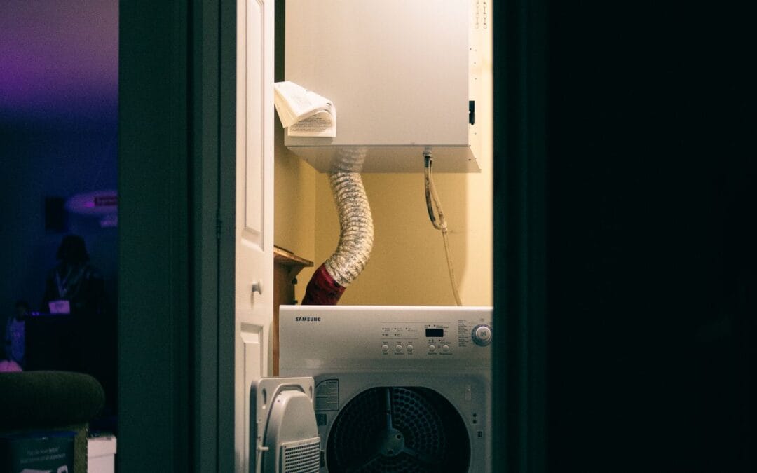 A vented tumble dryer in a laundry cupboard, with its exhaust hose running up the wall